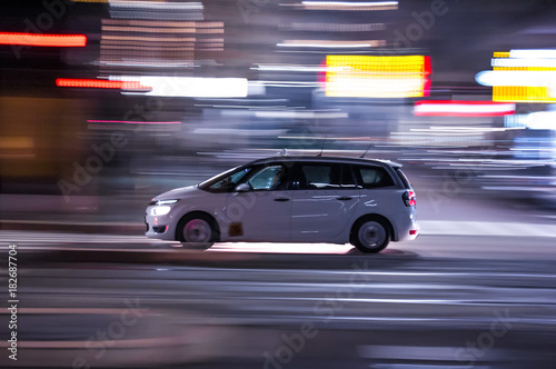 Automobile che sfreccia veloce di notte per le vie con luci colorate di una grande città 