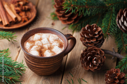 Spiced hot cocoa with marshmallows on rustic wooden table decorated pine cone and fir tree.