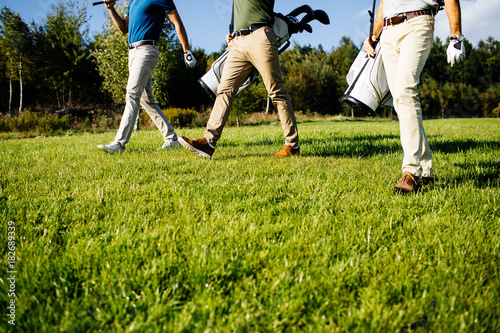 Golf player walking and carrying bag on course during summer game golfing