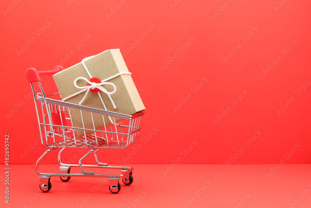 brown gift box in shopping cart on red paper background
