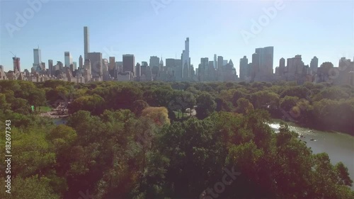 Aerial shot of New York Central Park, camera moving left over a lake, city view behind the trees. Concept of a green zone in a city