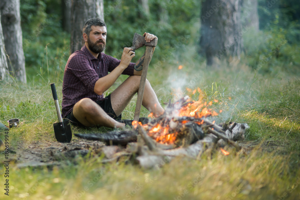 Man lumberjack with beard sharpen axe at bonfire
