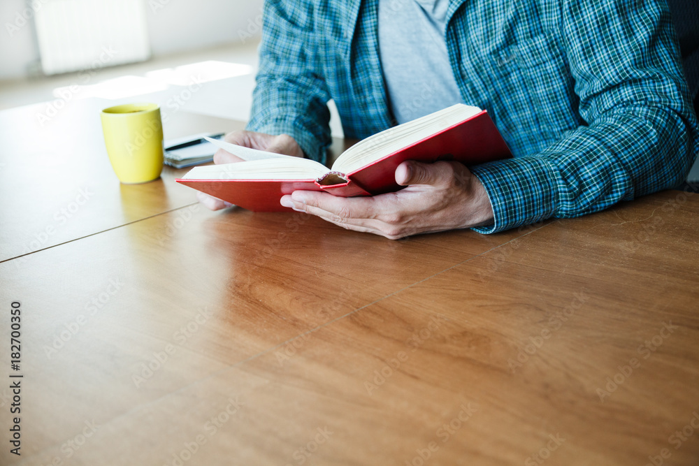 Obraz premium man reading book with cup of tea or coffee at home
