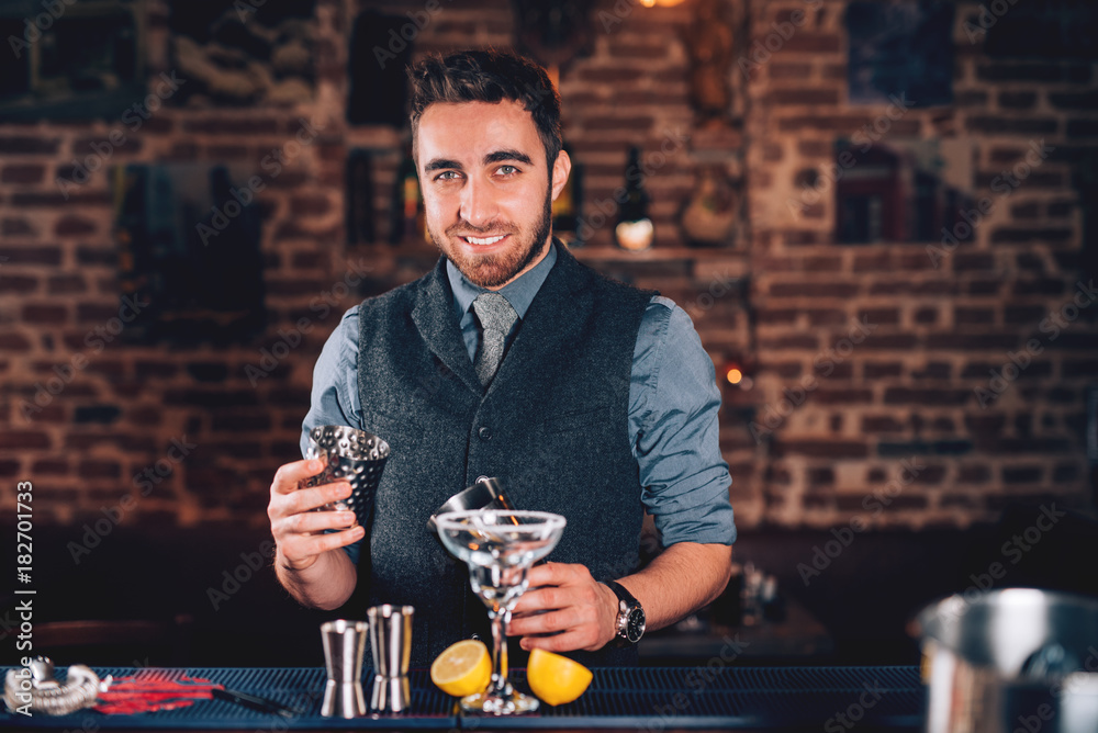 Smiling barman, professional waiter looking at camera and preparing cocktail