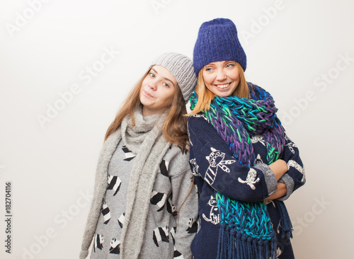 Two girls in winter clothes laughing on white background