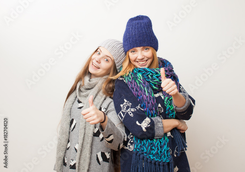 Two girls in winter clothes laughing on white background