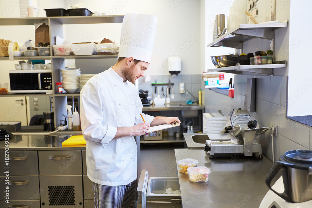 Obraz premium chef with clipboard doing inventory at kitchen