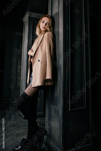 Portrait of young attractive pretty blonde woman in the beige jacket and leather shirt, gaiters, patent shoes on the dark background © k8most