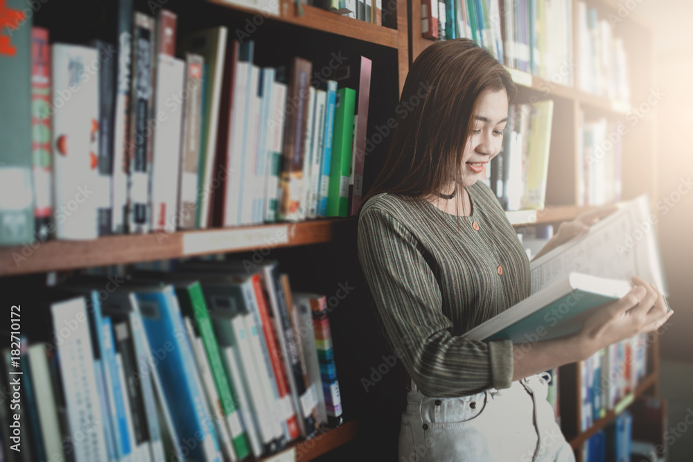 Young women reading book and stand front bookshelf in the library. Young women reading book and stand front bookshelf in the library.