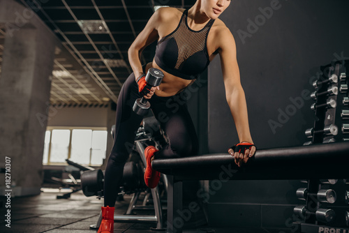 Keeping her body fit. Close-up of beautiful young woman with fit body exercising with dumbbells while standing against black background