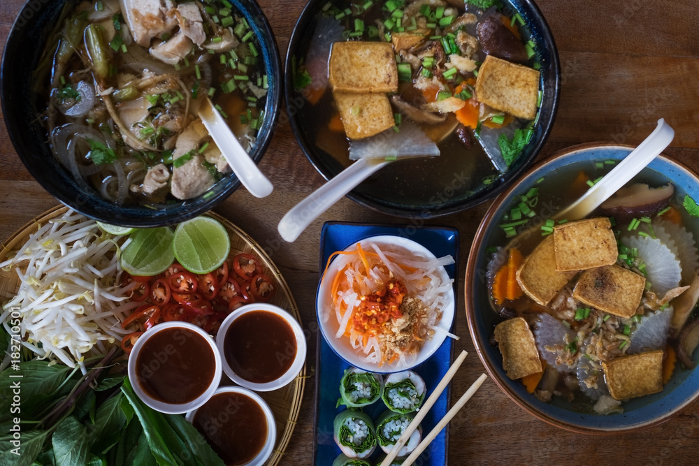 Traditional Vietnamese food. Soups, rolls and fresh herbs. Plates on a wooden surface. View from top to bottom.