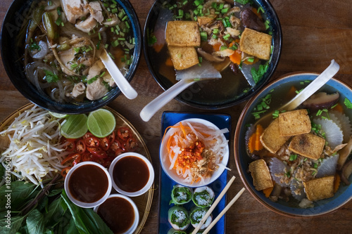Traditional Vietnamese food. Soups, rolls and fresh herbs. Plates on a wooden surface. View from top to bottom.