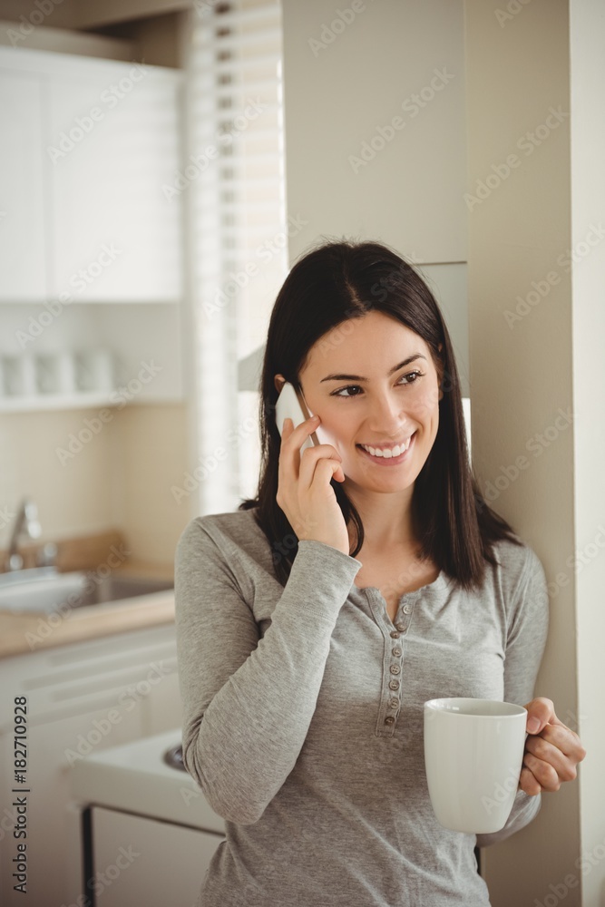 Smiling woman talking on mobile phone while holding coffee mug Smiling woman talking on mobile phone while holding coffee mug
