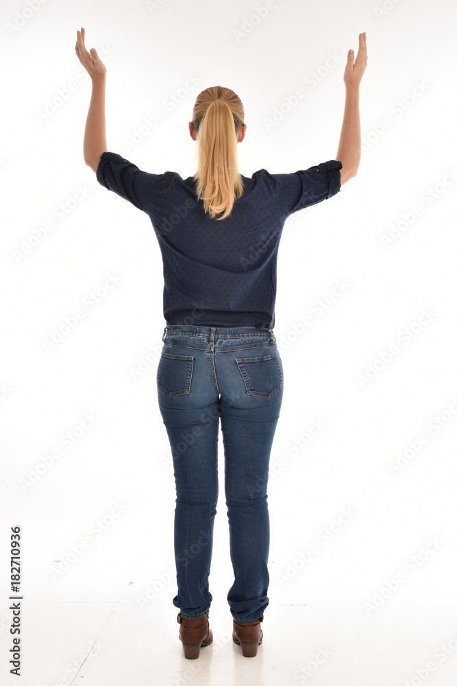 Full length portrait of a girl wearing simple blue shirt and jeans, standing pose facing away on a white background.