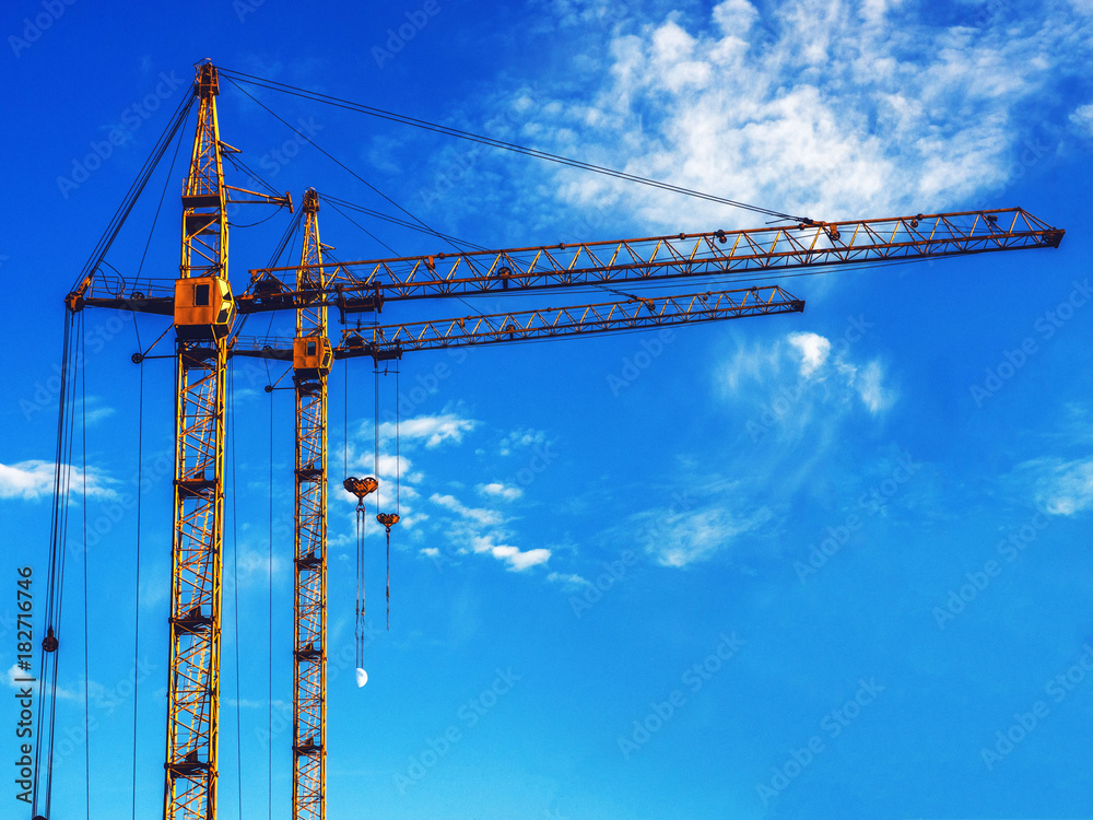 Two construction cranes against the blue sky. Place for your inscription on the right. Two construction cranes against the blue sky. Place for your inscription on the right.