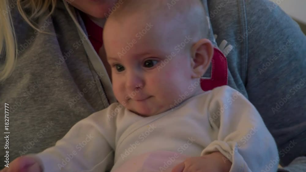 Young mom is pulling down dirty pink baby`s pants meanwhile little baby girl is sitting in mom`s lap.