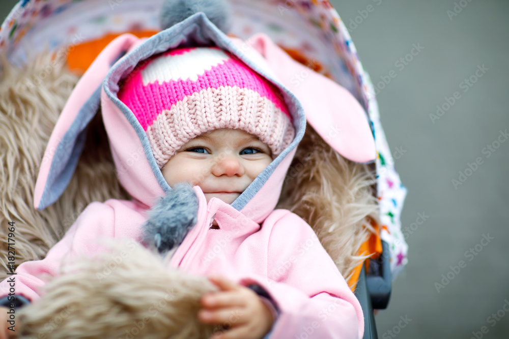 Cute little beautiful baby girl sitting in the pram or stroller on autumn day Cute little beautiful baby girl sitting in the pram or stroller on autumn day