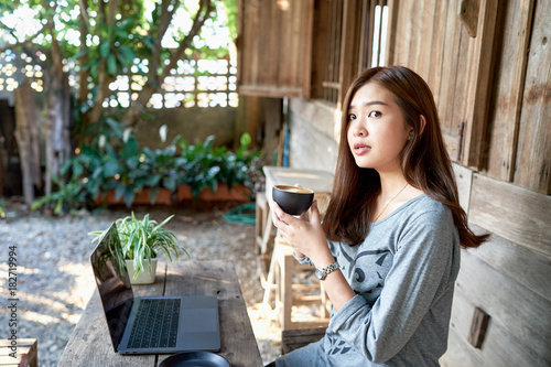 Portrait of young freelancer asian girl using laptop interrupted by something interested while drinking coffee