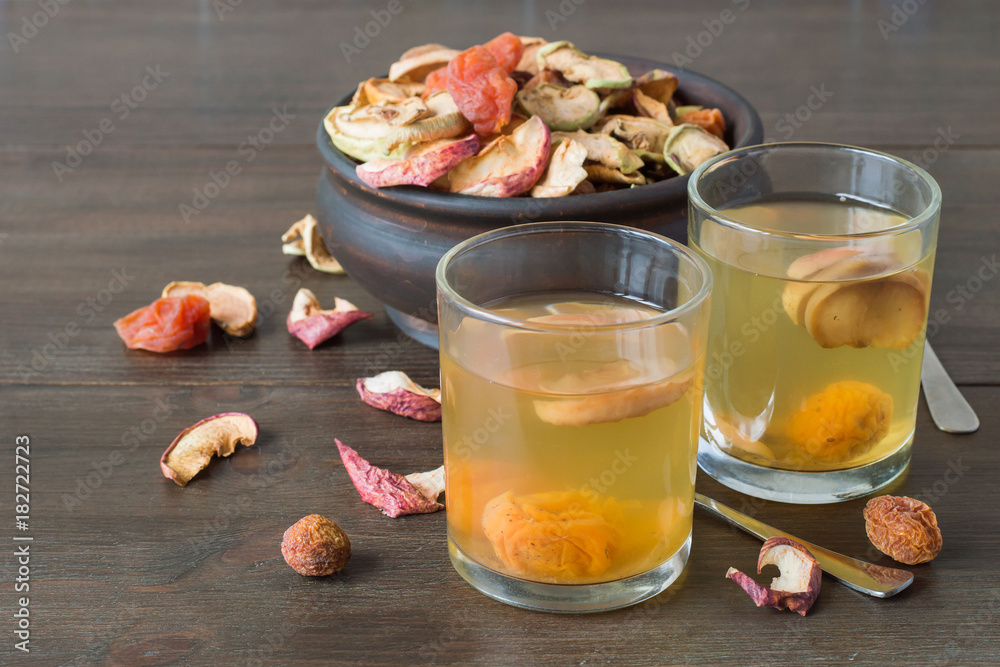 A mixture of dried fruits in a round wooden bowl and freshly prepared compote in a glass on a old table. Delicious and healthy drink. A mixture of dried fruits in a round wooden bowl and freshly prepared compote in a glass on a old table. Delicious and healthy drink.