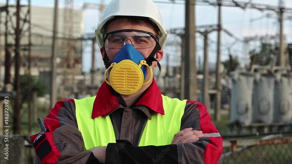 Worker in respirator on electric power station looks at the camera. Power engineering specialist in gas mask, goggles and hard hat at heat power plant Worker in respirator on electric power station looks at the camera. Power engineering specialist in gas mask, goggles and hard hat at heat power plant