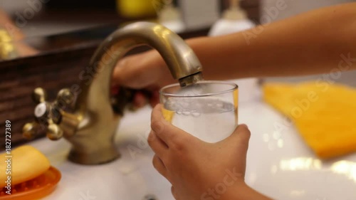 Child hands filling glass with water at the bathroom faucet - camera closing in photo