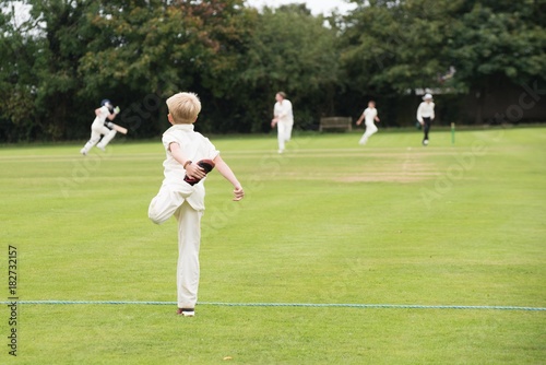 young player warms up by stretching in preparation for game of school cricket on English village green 