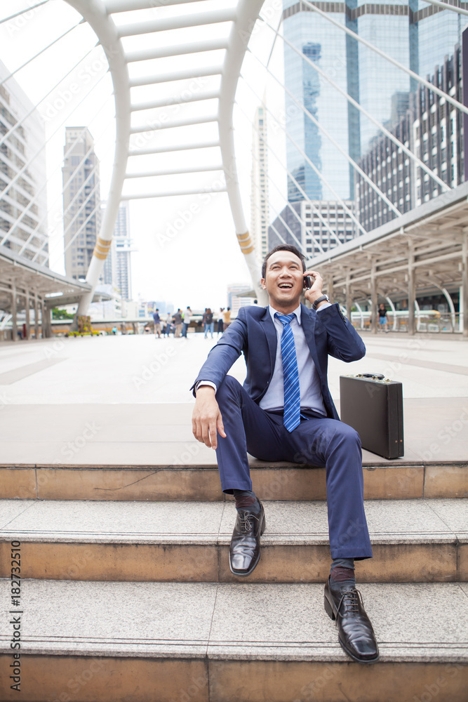 Businessman sitting on stair during callling the phone, with office building background - business success, achievement, and win concepts Businessman sitting on stair during callling the phone, with office building background - business success, achievement, and win concepts