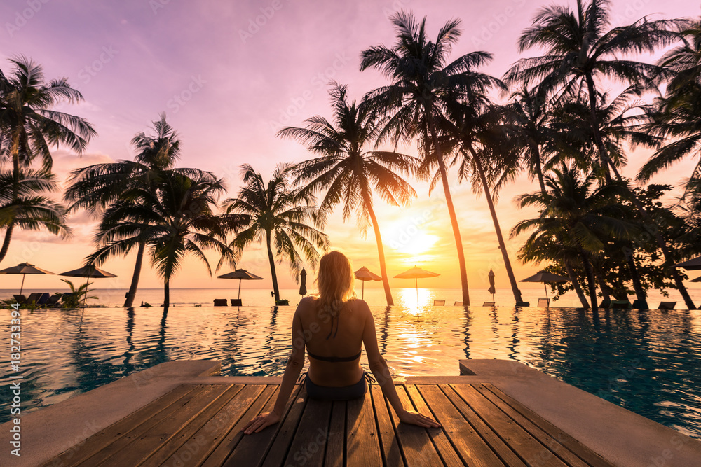 Fototapeta premium Woman relaxing by the pool in luxurious beachfront hotel resort