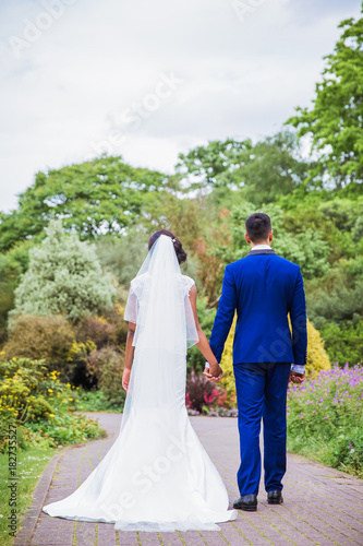 Back view of young happy newlyweds who holding hands each other in the park