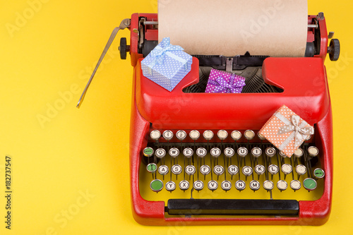 Holidays concept - red typewriter with blank craft paper, gift boxes on yellow background