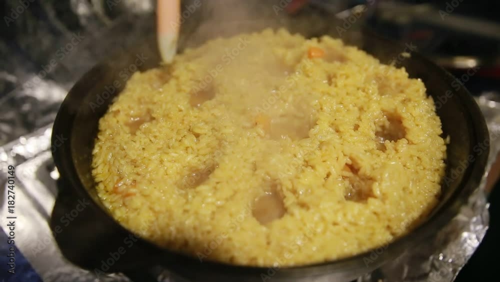 Cooking pilaf, shef makes holes for the boiling of the pilaf in cast-iron kettle