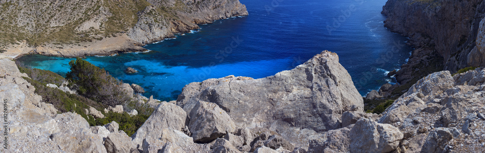 A panoramic picture of clear bright blue waters surrounded with rocky mountainous landscape