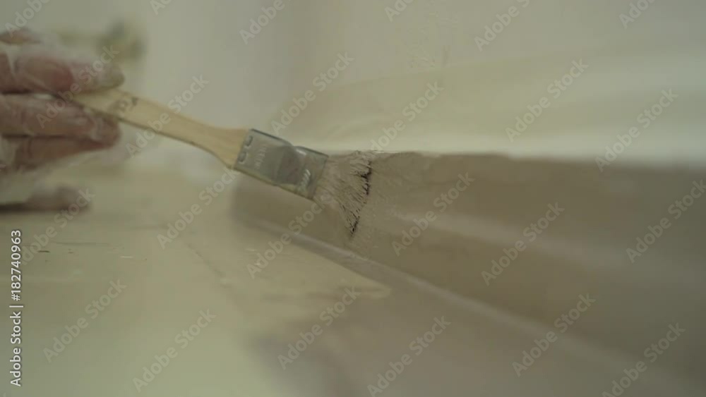 Hand painting floor and skirting board with paint brush and light brown paint CLose up