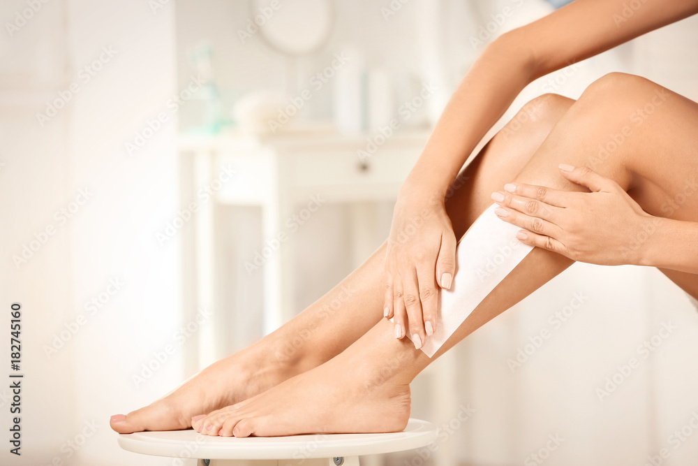 Fototapeta premium Beautiful woman waxing her legs in bathroom