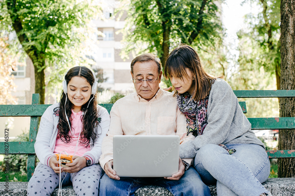 .A father with his daughters sitting on a stone bench, learning to use the laptop. Relaxed autumn day in family outdoors. Lifestyle portrait... .A father with his daughters sitting on a stone bench, learning to use the laptop. Relaxed autumn day in family outdoors. Lifestyle portrait...
