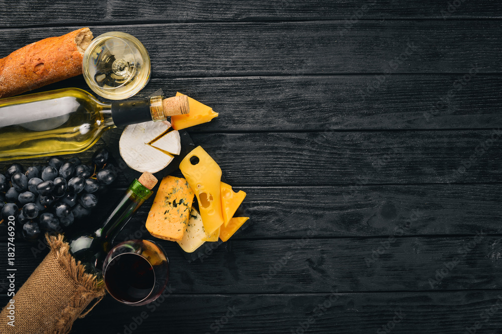 A bottle of wine, grapes and cheese on a wooden background. Cheese brie, blue cheese, gorgonzola, fuete, salami. Italian Traditional Cuisine. Free space for text. Top view.