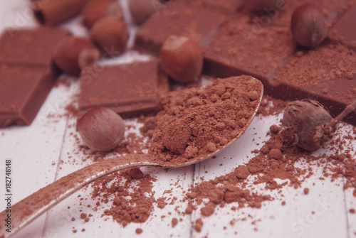 Brown Chocolate Powder on a Spoon Over a wooden table with Nuts and Chocolate Bar.