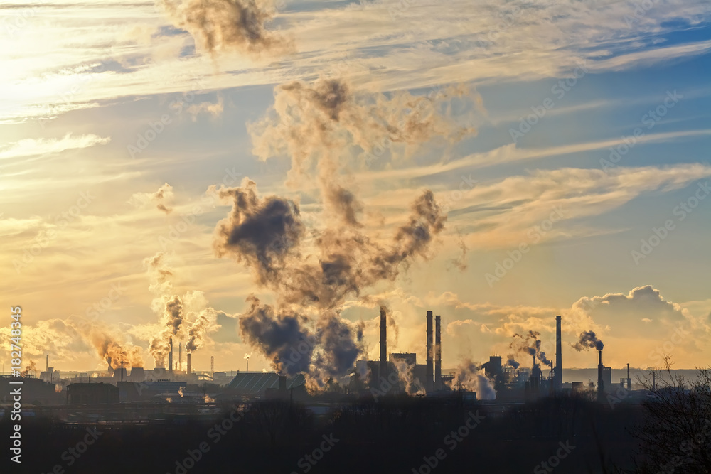 the pipes of a large plant smoke in the sky