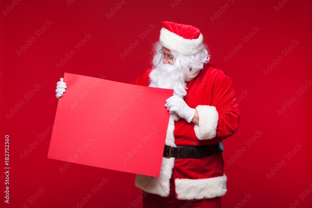 Naklejka premium Santa Claus pointing in blank advertisement banner isolated on red background with copy space red leaf