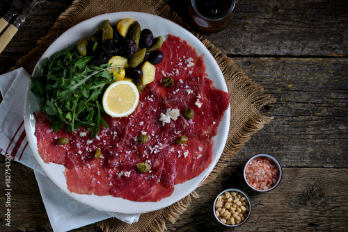 Beef carpaccio with parmesan, arugula, pickled cucumbers, squash, dried olives, and capers.