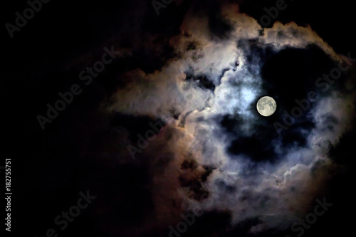 The moon illuminates the black sky around its light at night. Copy space for text. The moon behind the clouds.