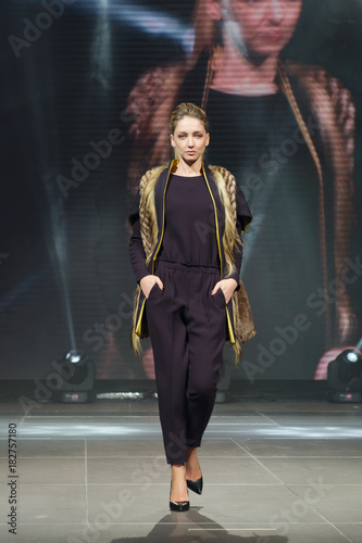 Obraz na plátně Beautiful fashion model  walks on runway in fur coat with online screen on backg
