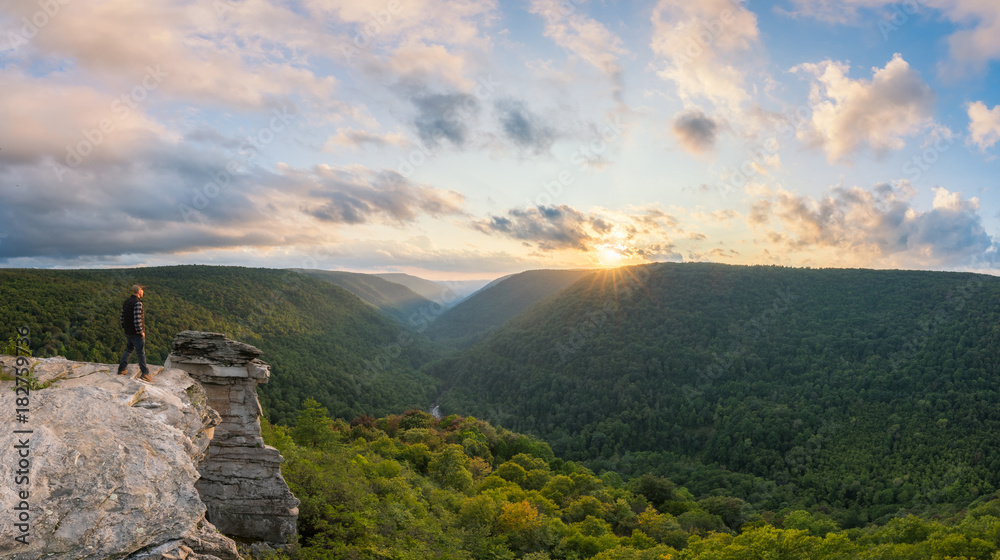 Hiker watches the setting sun from the edge of a cliff 