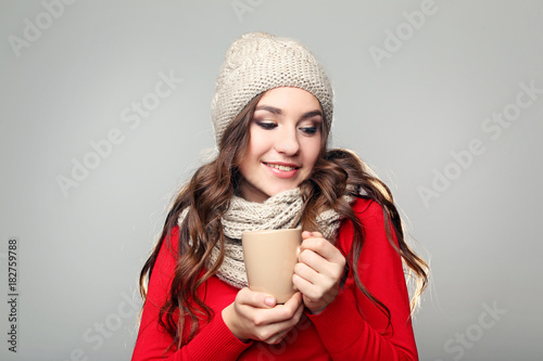 Beautiful young girl in hat and scarf holding cup of tea