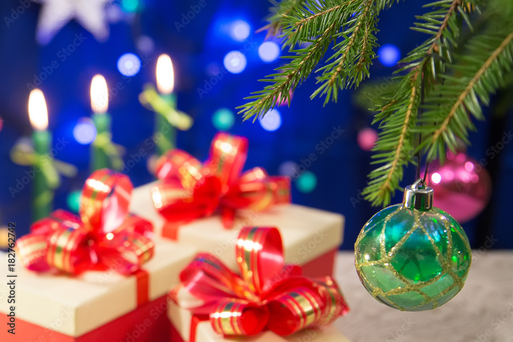 a fragment of a New Year tree decorated with beautiful balls. on the table are New Year's gifts. Burning candles on a dark blue background with blurred lights. horizontal. a fragment of a New Year tree decorated with beautiful balls. on the table are New Year's gifts. Burning candles on a dark blue background with blurred lights. horizontal.