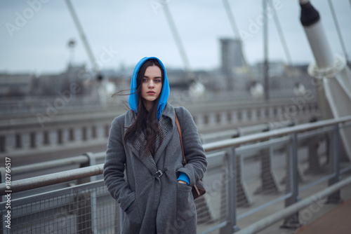 Young woman in the coat, walks on the city bridge during the windy weather. Urban autumn winter style photo