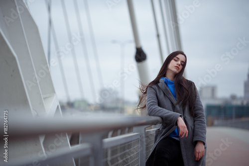 Young woman in the coat, walks on the city bridge during the windy weather. Urban autumn winter style © Iulia