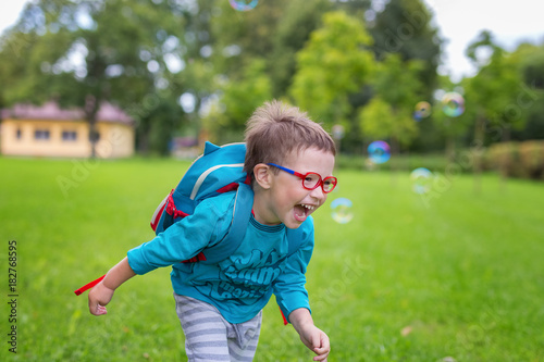 Young happy boy running in the grass at the park on a summer day