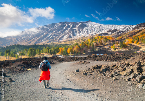 Hiker on a lavic path in the northern side of Mount Etna, Italy, and the snowy volcano