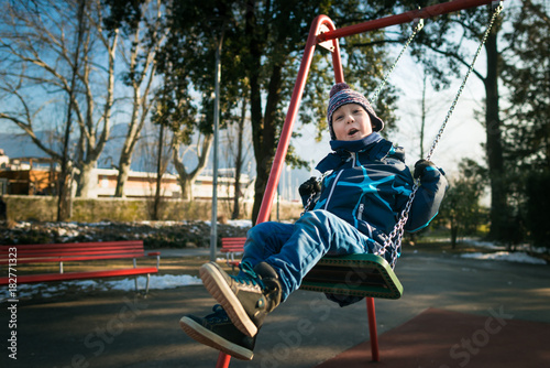 Happy little boy on swing in beautiful winter day have fun and makes faces